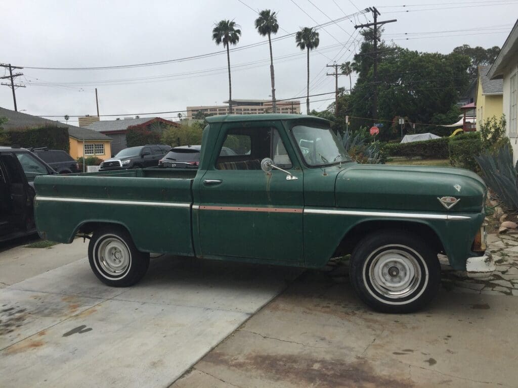 Vintage green pickup truck parked in a driveway under cloudy sky.