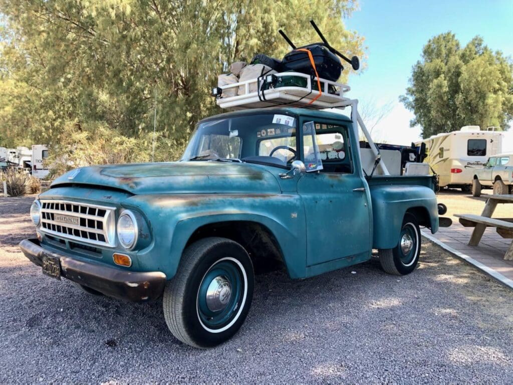 Vintage blue pickup truck with luggage on the roof parked outdoors.