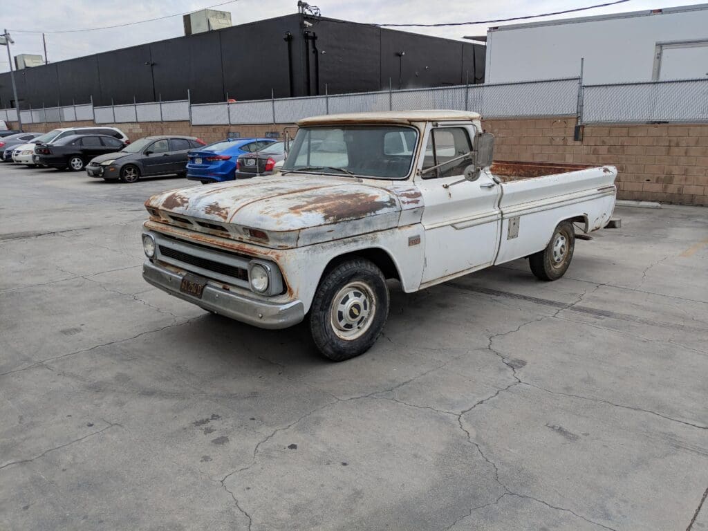 Rusty vintage pickup truck parked in an industrial lot.