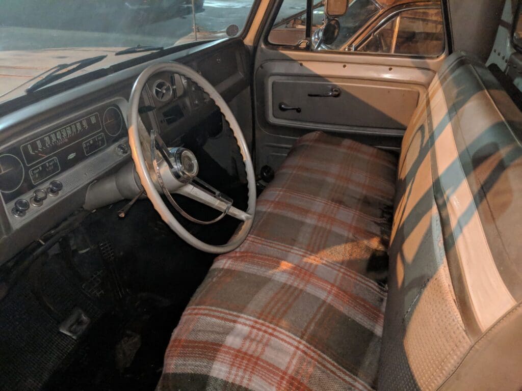 Interior of a vintage car with plaid seats and a classic steering wheel.