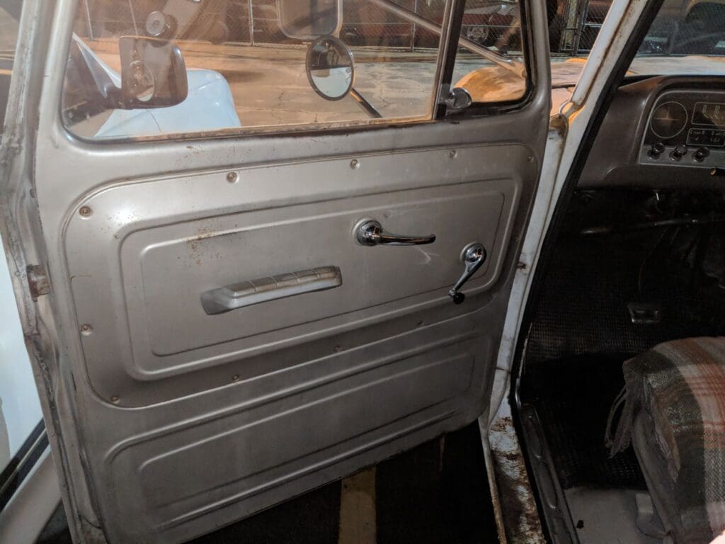 Interior view of a vintage car door with manual window controls.
