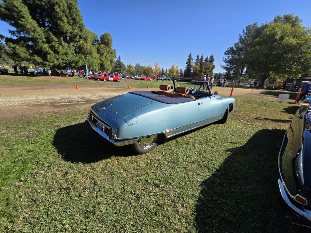 A classic blue convertible car with its top down parked on grass.
