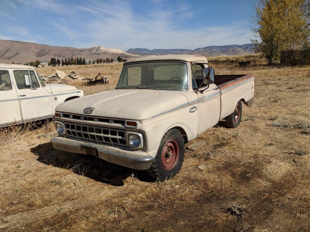 Old white pickup truck parked in a dry field under a blue sky.
