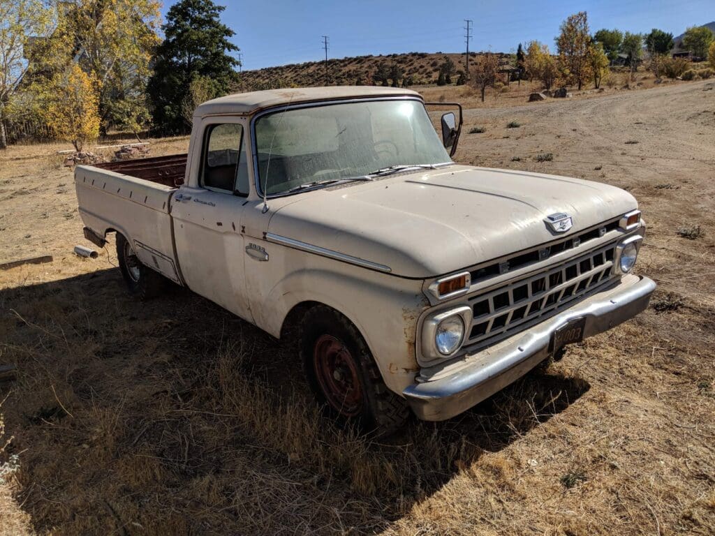 Old white pickup truck parked on dry grass in a rural area.