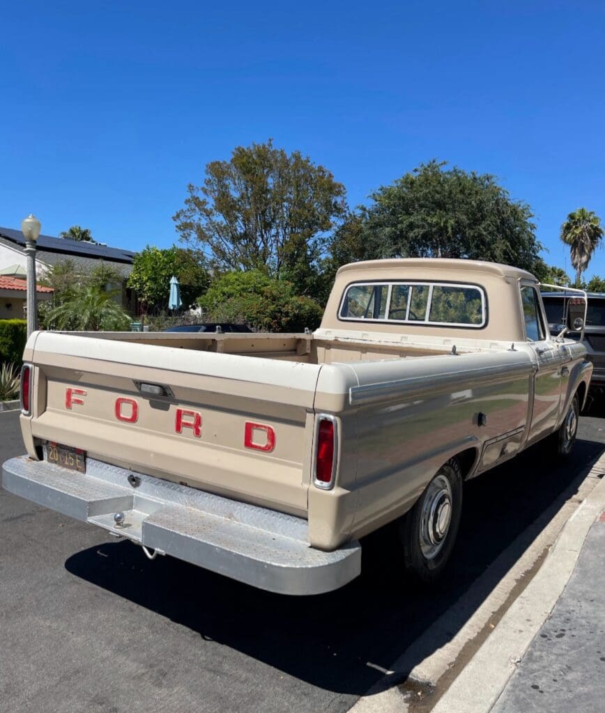 Old white pickup truck parked on dry grass in a rural area.