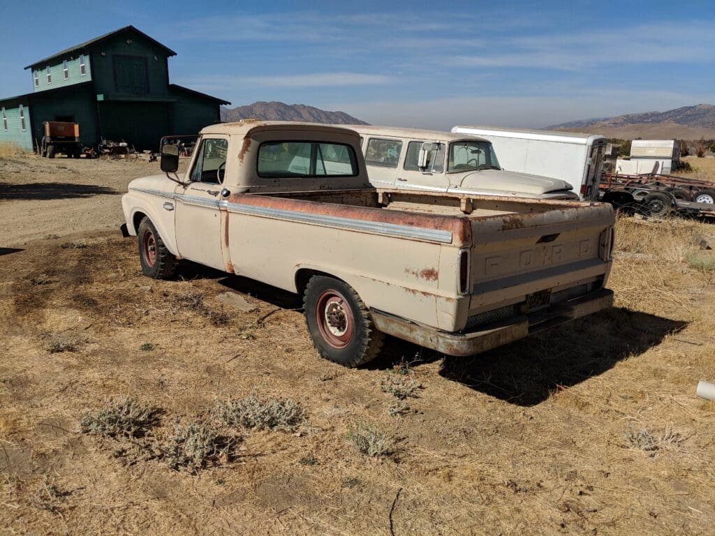 Old white pickup truck parked on dry grass under blue sky.