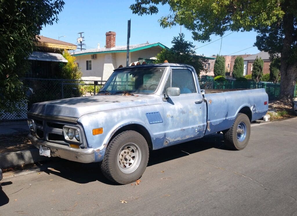Old blue pickup truck parked on a sunny street.