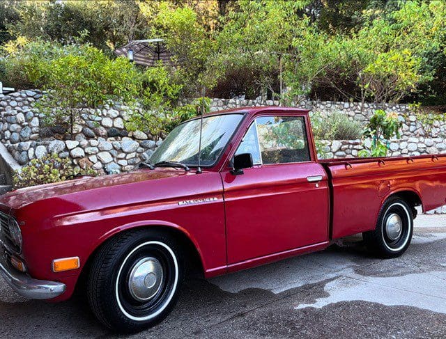 A classic red pickup truck parked outdoors near a stone wall.