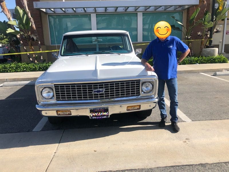 Man standing next to a vintage white Chevrolet truck in a driveway.