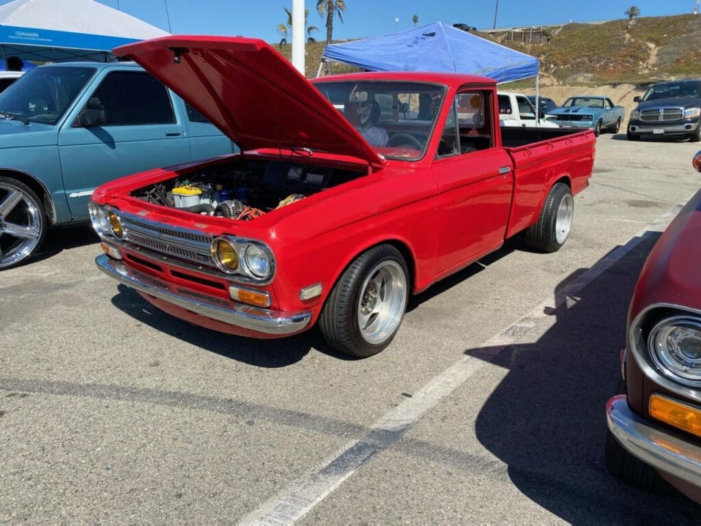 Classic red pickup truck with hood open at a car show.