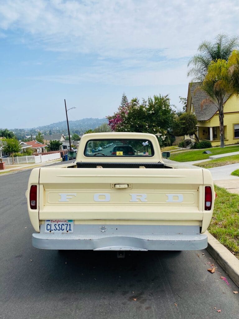Rear view of a vintage cream-colored pickup truck parked on a suburban street.