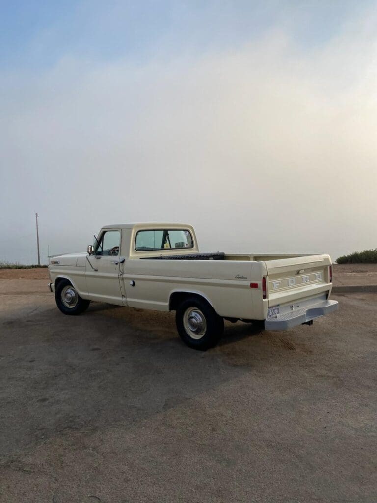 Classic beige pickup truck parked on a dusty road under a hazy sky.