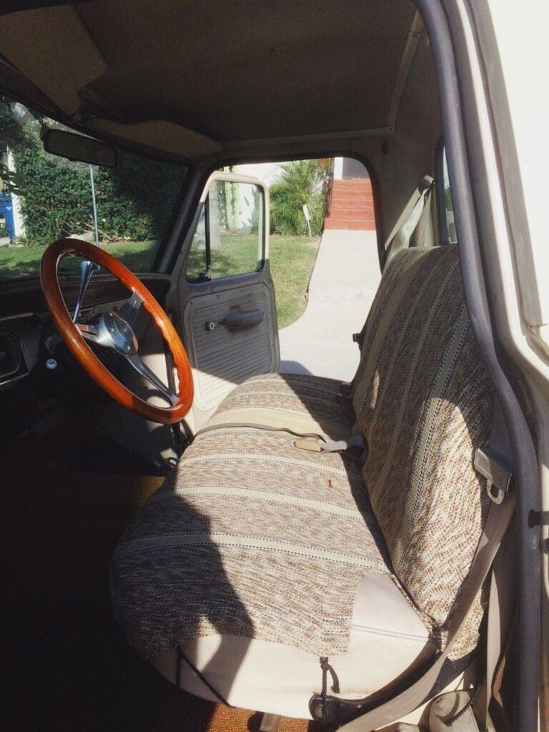 Interior view of a vintage car with patterned seats and a wooden steering wheel.