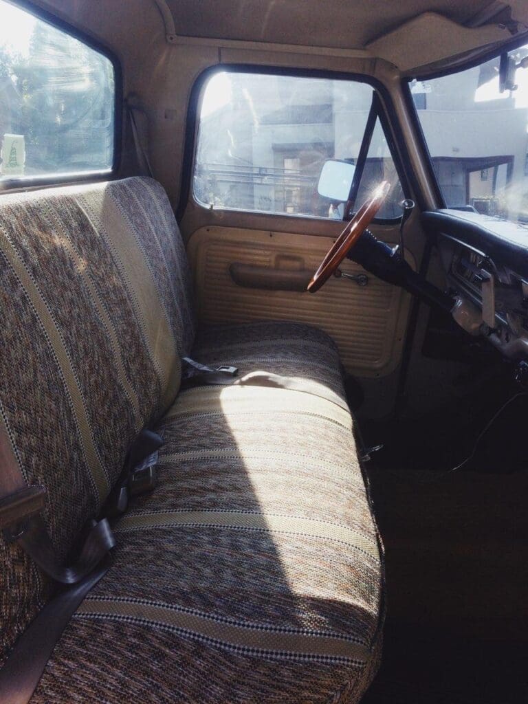 Vintage car interior with patterned bench seat and classic steering wheel.