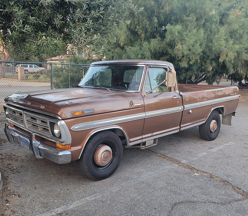 A vintage brown pickup truck parked outdoors near trees.