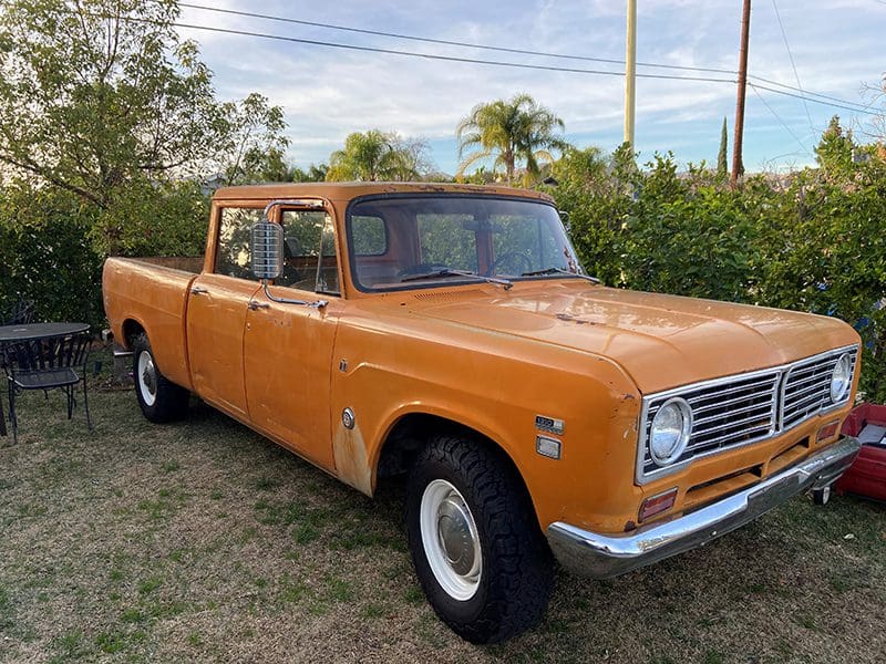 Vintage orange pickup truck parked outdoors on grass.