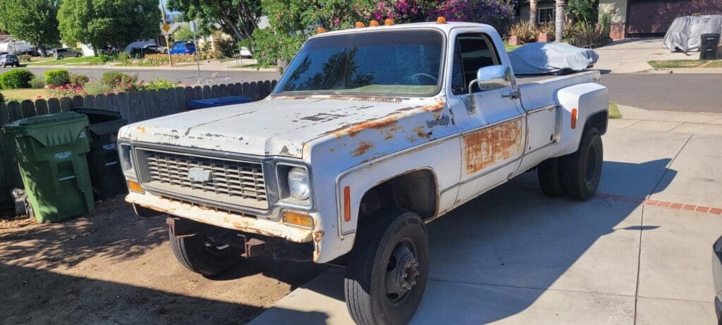 Rusty white pickup truck with weathered paint and missing front bumper.