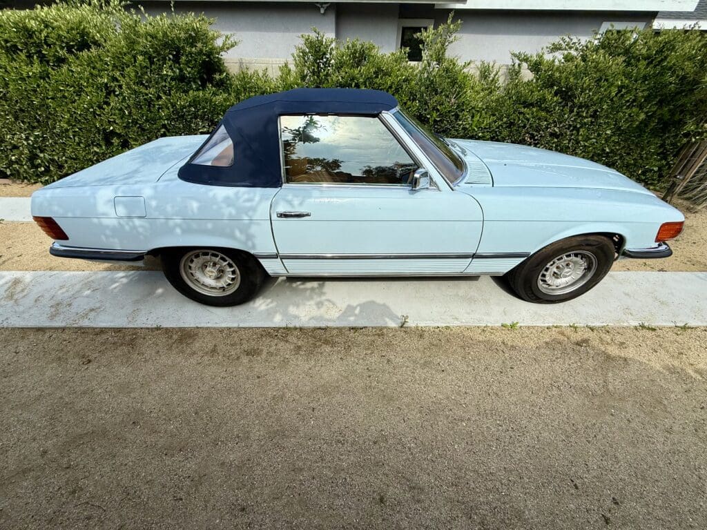Light blue vintage convertible parked by a hedge.