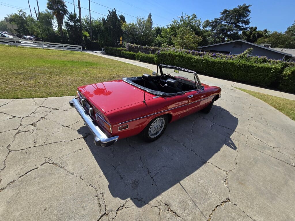 Red convertible car parked on a sunny driveway with a green lawn.