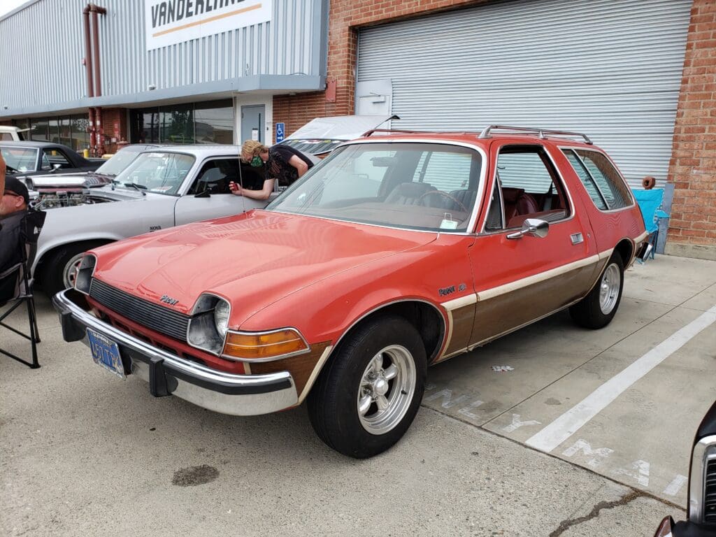 Classic red AMC Pacer parked outside a building with a vintage vibe.