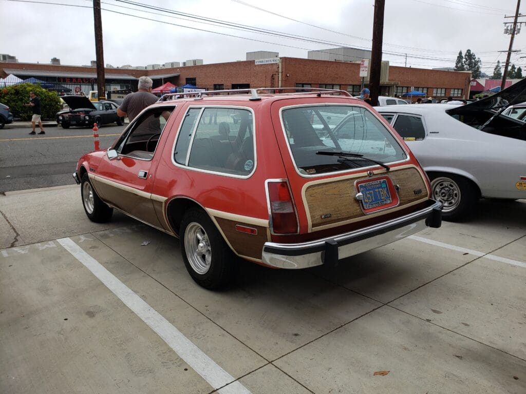 Classic red AMC Pacer parked outside a building with a vintage vibe.