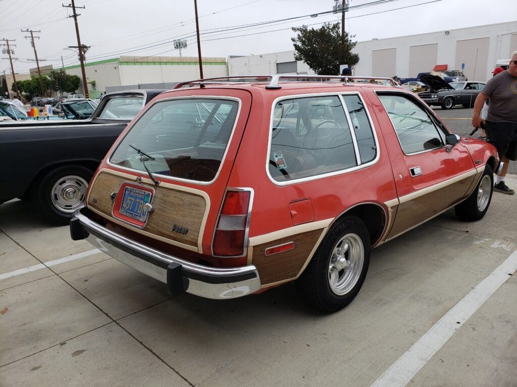 Classic red AMC Pacer parked outside a building with a vintage vibe.