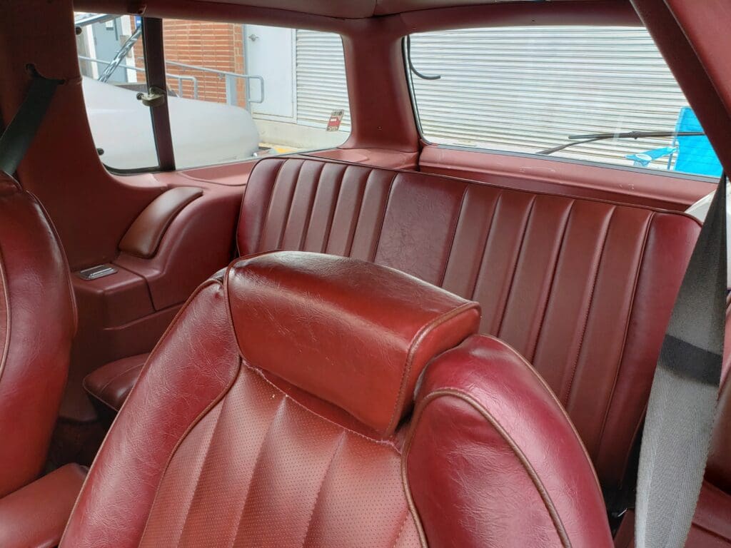 Interior of a vintage car with red leather seats and a headrest.