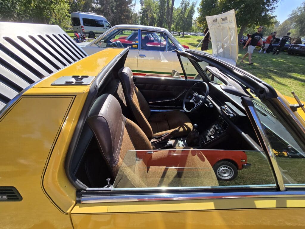 Yellow vintage car with open door showcasing brown leather interior.