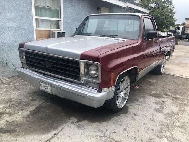 Classic maroon pickup truck with shiny chrome wheels parked outside a house.
