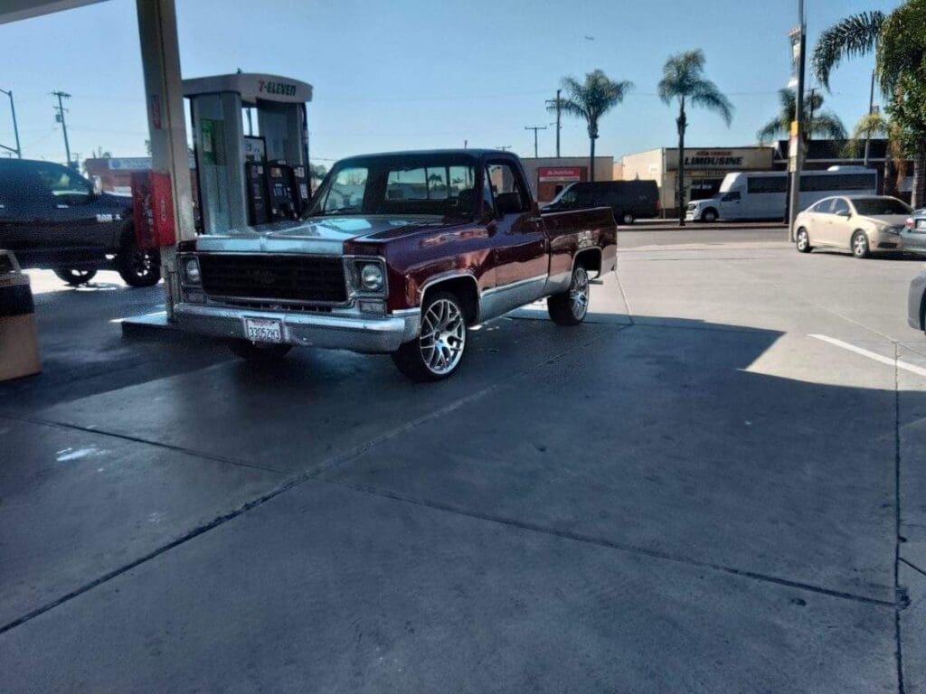 Classic black pickup truck parked at a gas station on a sunny day.