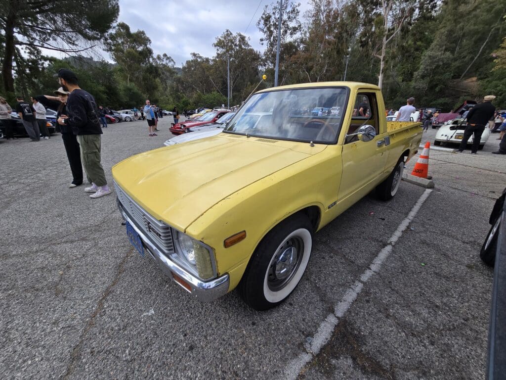 Yellow vintage pickup truck parked at an outdoor car show.