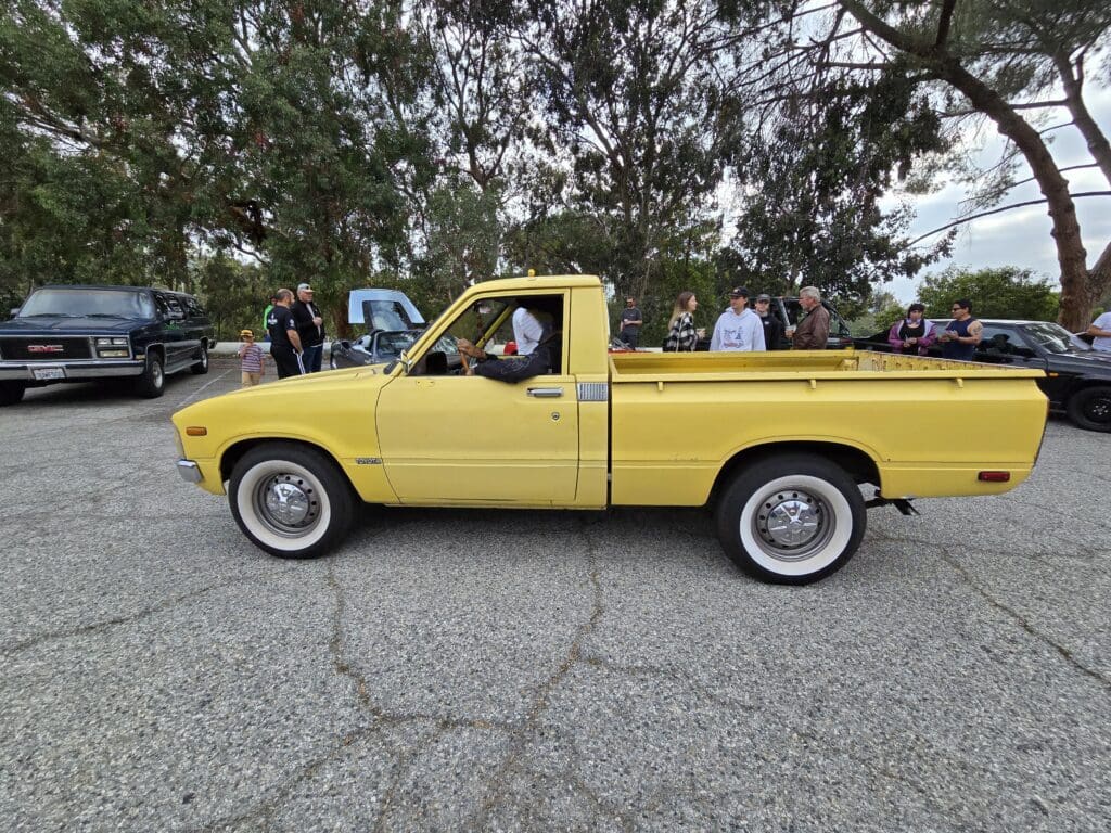 Yellow vintage pickup truck parked on a road with people nearby.