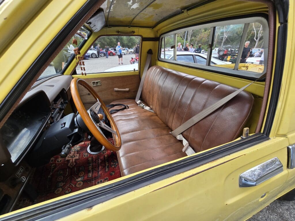 Interior of a vintage yellow car with brown leather bench seat and wooden steering wheel.