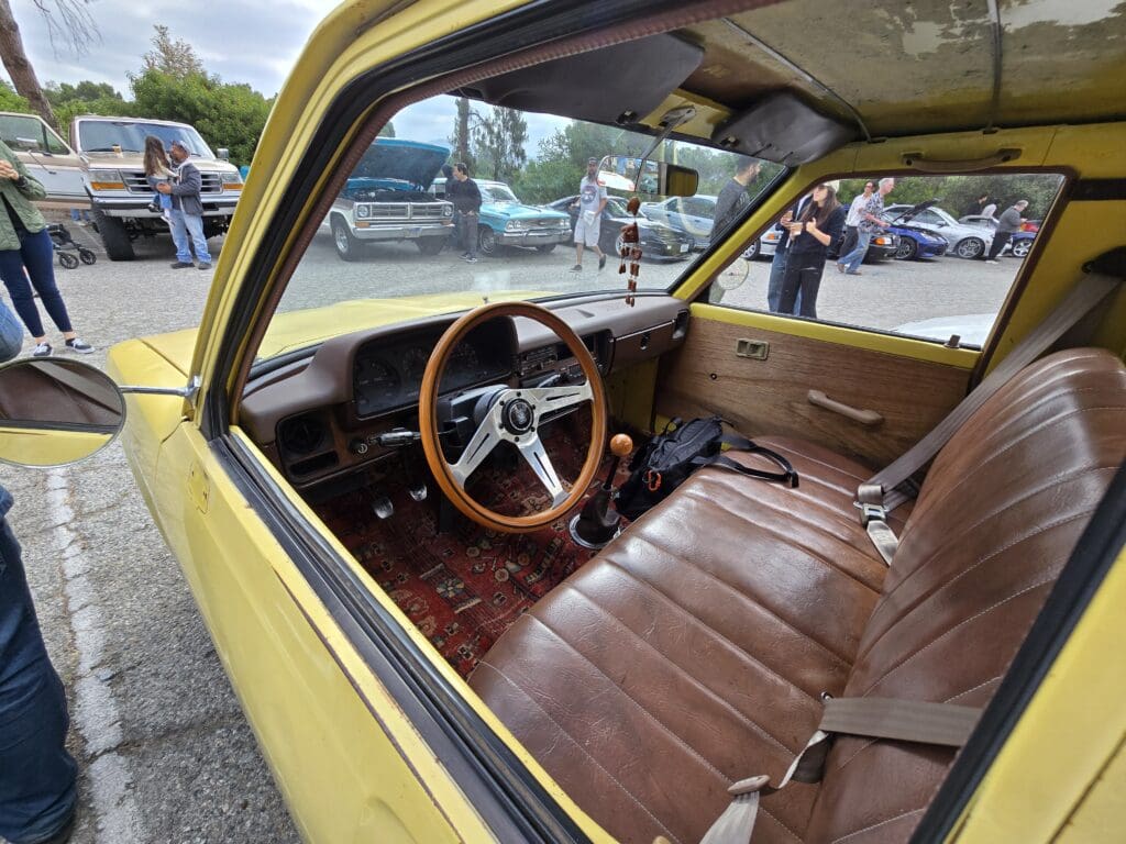 Interior of a vintage yellow car with brown leather seats and a wooden steering wheel.