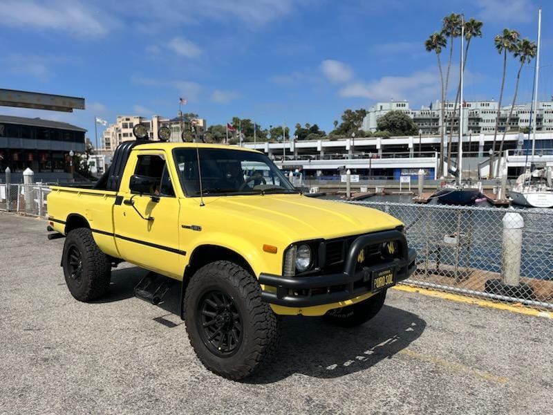 Yellow lifted pickup truck parked near a marina with boats.