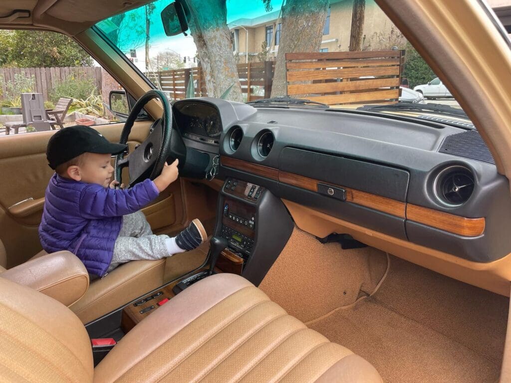 A child sitting in the driver's seat of a vintage car, gripping the steering wheel.