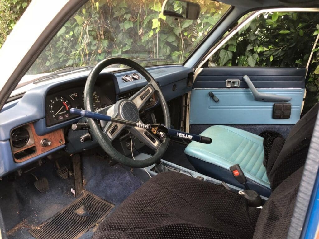 Interior of a vintage car with blue seats and a classic steering wheel.