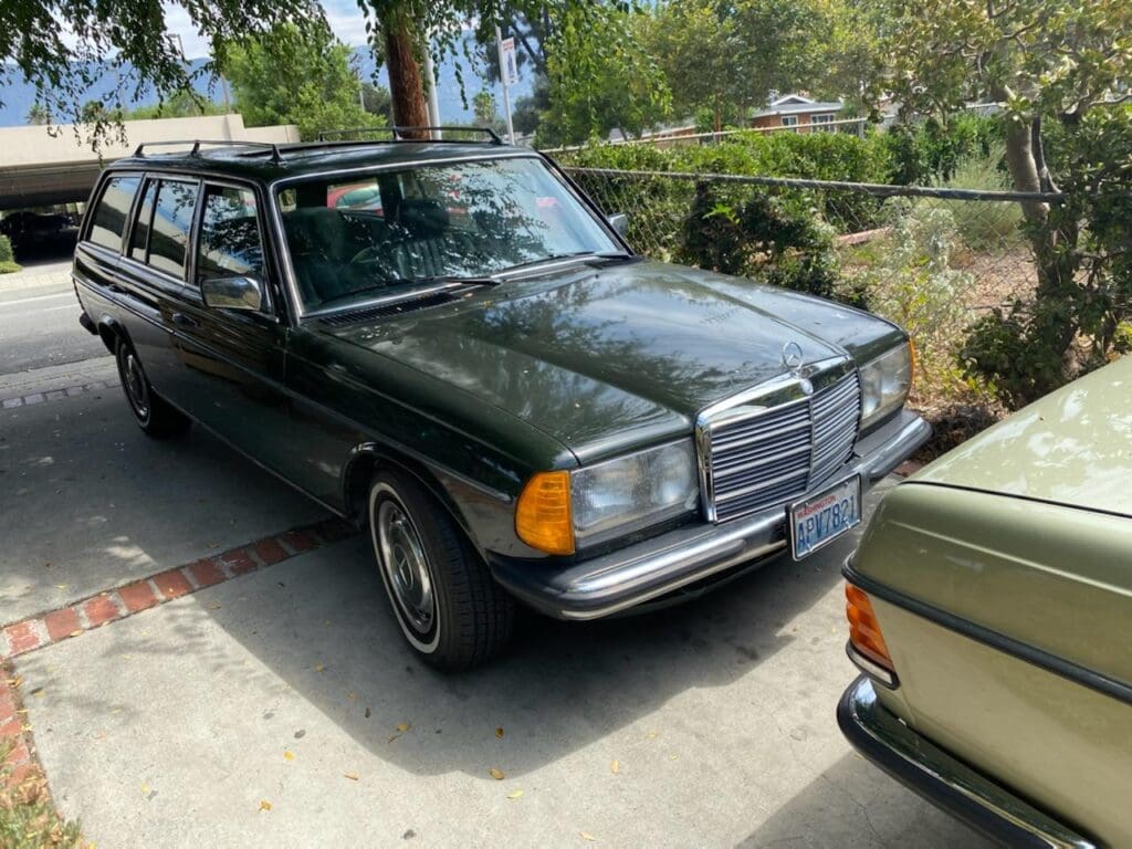 Classic dark green Mercedes-Benz parked outdoors next to another vintage car.