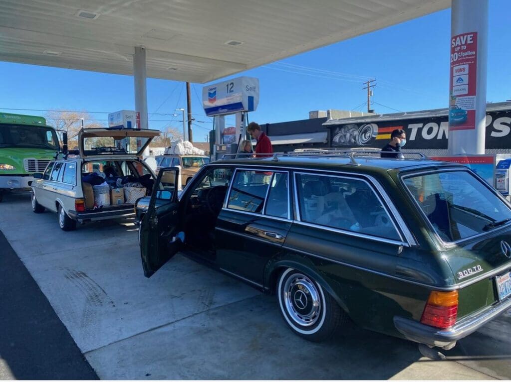 A vintage station wagon at a gas station with its door open.