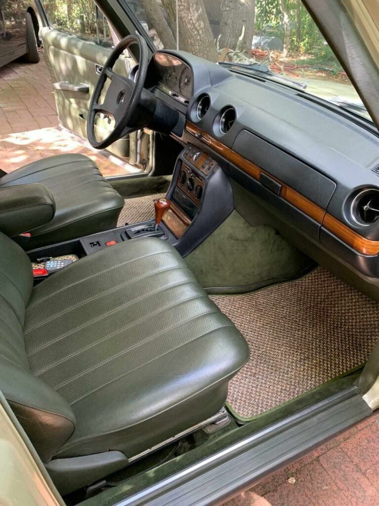 Interior view of a classic car with green leather seats and wooden dashboard accents.