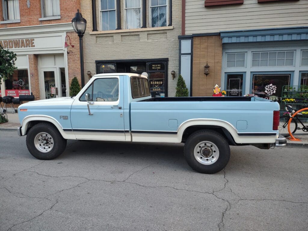 Light blue vintage pickup truck parked on a street in front of buildings.
