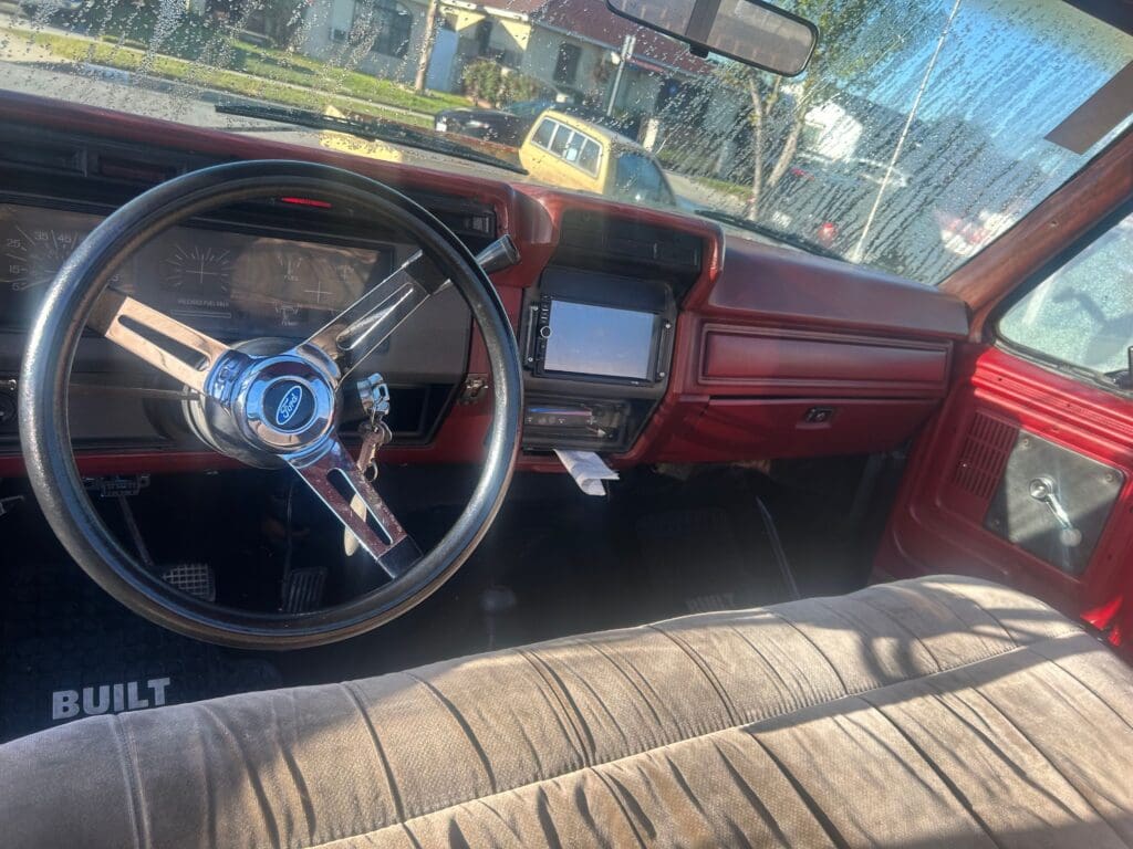 Interior of a vintage red car with a steering wheel and dashboard.