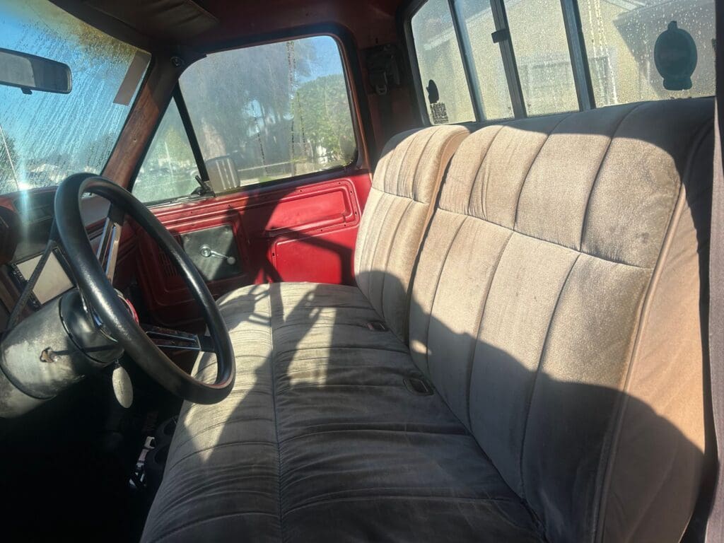 Interior view of an old truck with bench seating and a steering wheel.