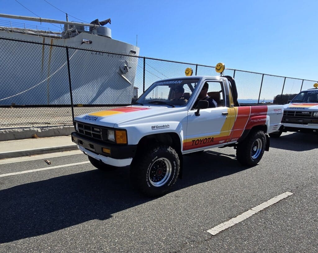 Vintage white pickup truck with red and yellow stripes parked by a waterfront.