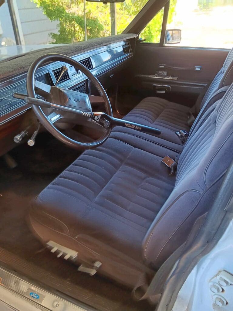 Interior of a vintage car with blue fabric seats and a wooden dashboard.
