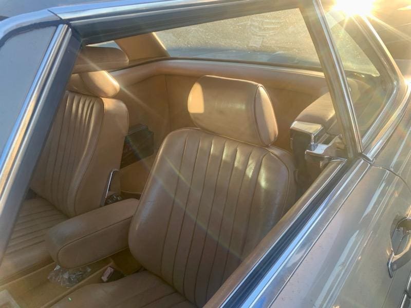Interior view of a classic car with brown leather seats and sunlight streaming through the window.