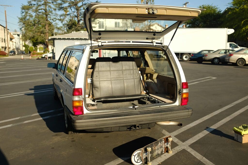 An old station wagon with its rear hatch open and a skateboard on the ground.