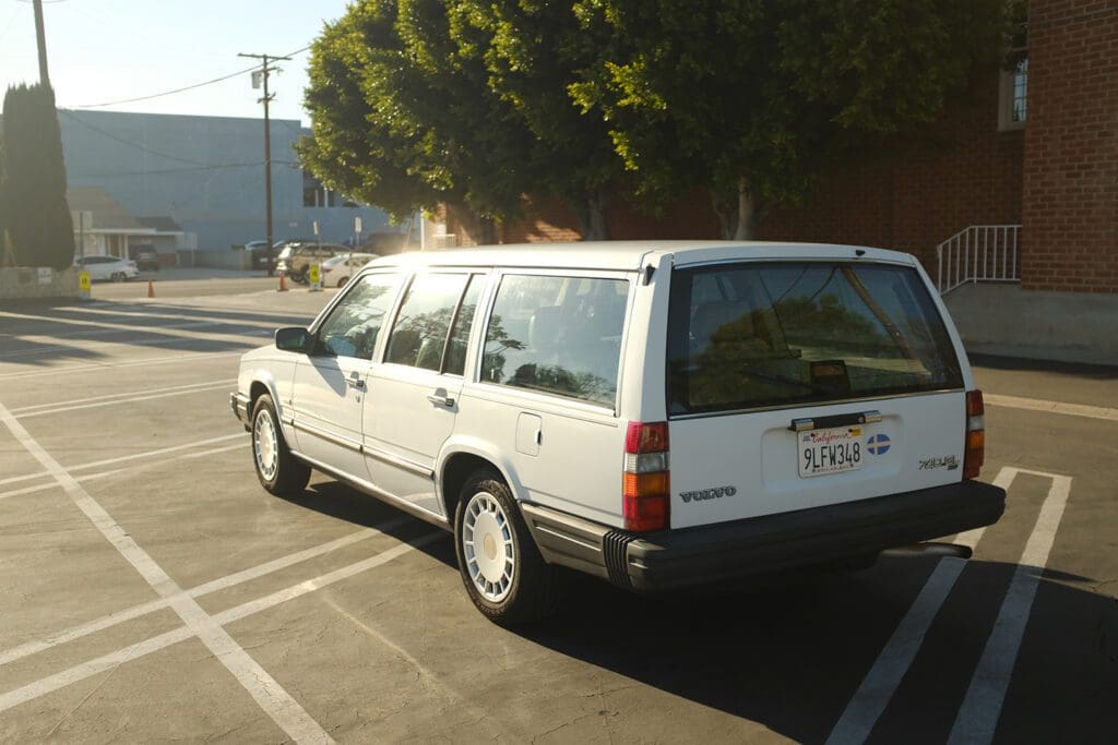 White station wagon parked in a lot under a tree.