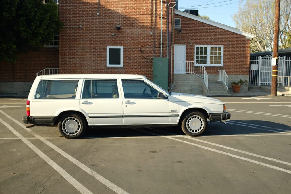 A white station wagon parked on the street near brick buildings.