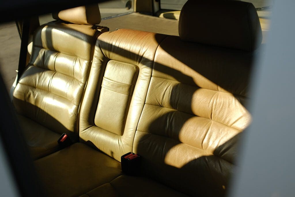 Sunlit tan leather car seats with visible stitching and headrests.